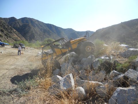 1986 Ford Bronco - An off-road vehicle navigates a challenging rocky terrain under a clear blue sky.