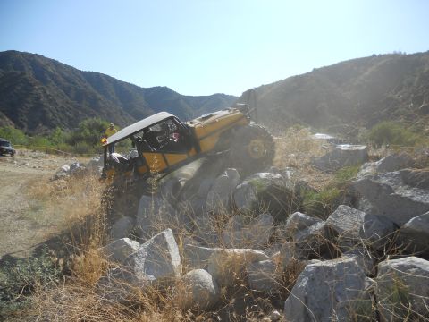 1986 Ford Bronco - A yellow off-road vehicle navigates a rocky terrain, with another vehicle visible in the background.