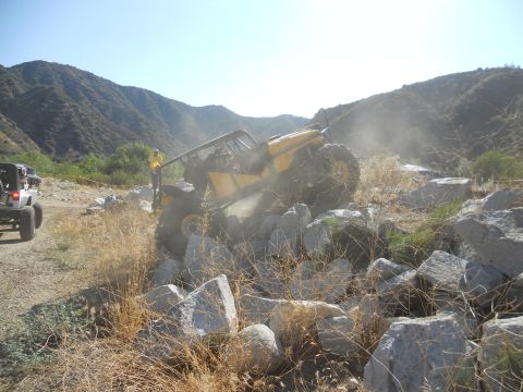 1986 Ford Bronco - An off-road vehicle attempts to climb over large rocks in a dry, mountainous area.