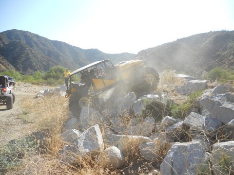 1986 Ford Bronco - A yellow off-road vehicle tackles a challenging rocky path, with another vehicle visible in the background.