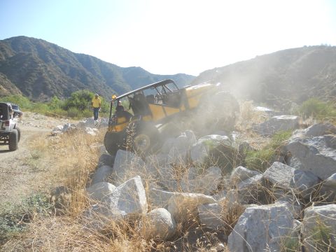 1986 Ford Bronco - An off-road vehicle navigates a rocky trail, kicking up dust, with another vehicle in the background.