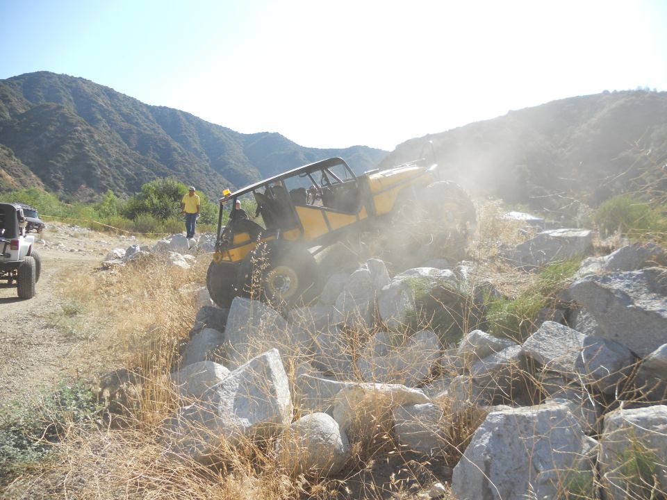 Yellow off-road vehicle climbing over rocks, another white SUV visible