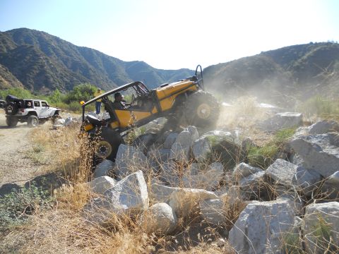 1986 Ford Bronco - Two off-road vehicles traverse a challenging rocky path in a mountainous area.