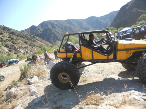1986 Ford Bronco - A group of off-road vehicles navigate a rocky mountain trail under a clear blue sky.