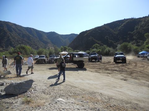 1986 Ford Bronco - Off-road vehicles gather in a dry riverbed with mountains in the background.