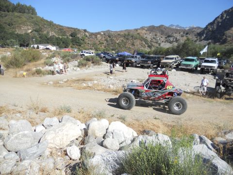 1986 Ford Bronco - A custom-built off-road buggy is parked on a dirt track, with a line of trucks and SUVs in the background.