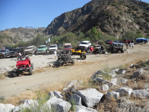 1986 Ford Bronco - Several off-road vehicles are gathered in a dusty, rocky area with a mountain range visible in the distance.