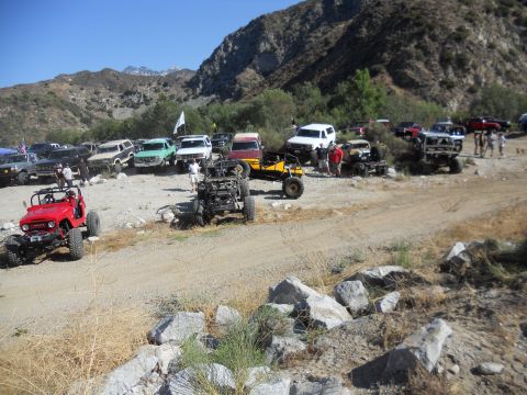 1986 Ford Bronco - A collection of off-road vehicles are parked in a dusty, arid landscape with mountains in the background.