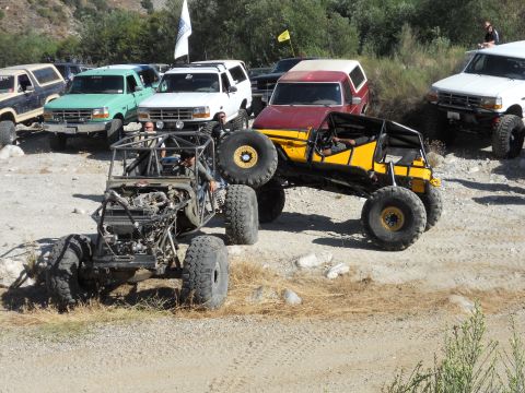 1986 Ford Bronco - Several off-road vehicles are gathered on a dirt lot, including a custom yellow buggy and a white Ford Bronco.