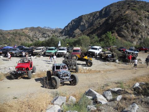 1986 Ford Bronco - A large group of off-road vehicles are gathered in a dry, mountainous area under a clear blue sky.