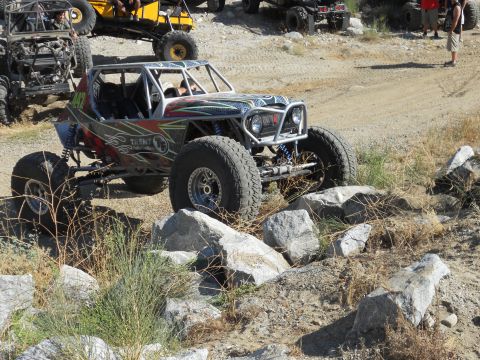 1986 Ford Bronco - A custom-built off-road buggy navigates a rocky trail, with other off-road vehicles visible in the background.