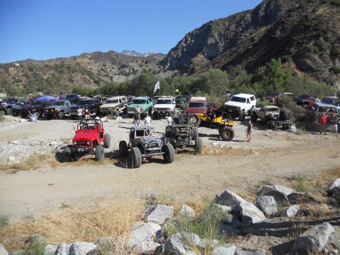 1986 Ford Bronco - A group of off-road vehicles are gathered in a dry riverbed with mountains in the background.