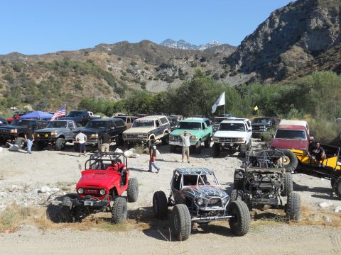 1986 Ford Bronco - Several off-road vehicles are gathered in a scenic, mountainous area under a clear blue sky.
