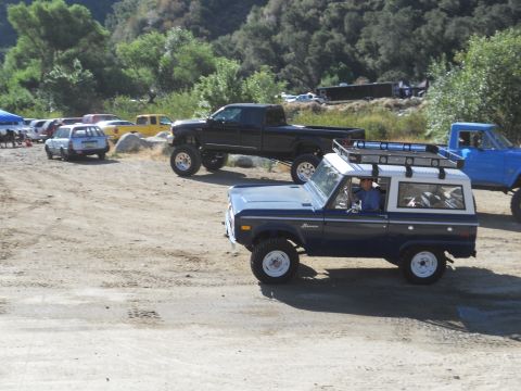 1986 Ford Bronco - A dark blue Ford Bronco with a white roof and roof rack is parked on a dirt lot with other vehicles.