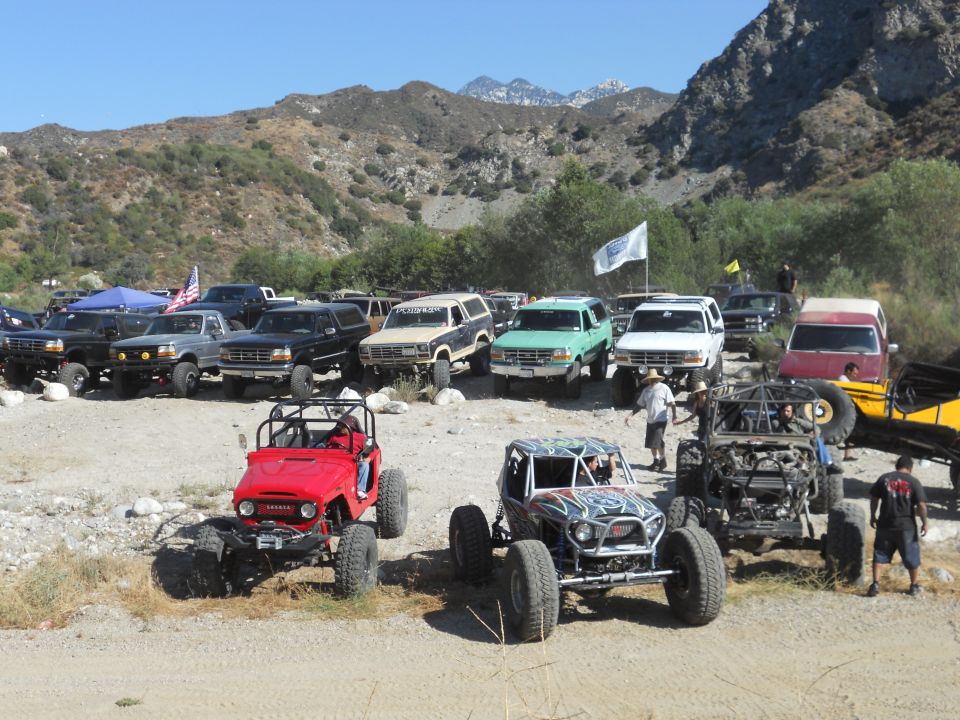 Several off-road vehicles, including a red Jeep-like buggy and a custom buggy, parked in a dusty area with mountains in the background
