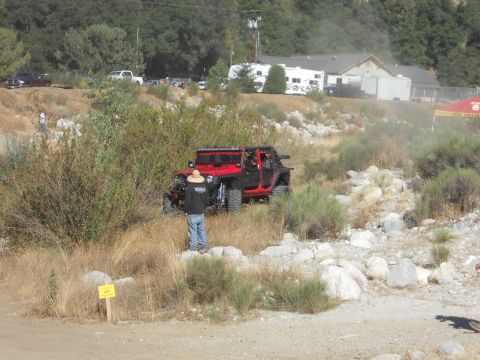 1986 Ford Bronco - A red Jeep navigates a rocky, off-road trail with spectators nearby.