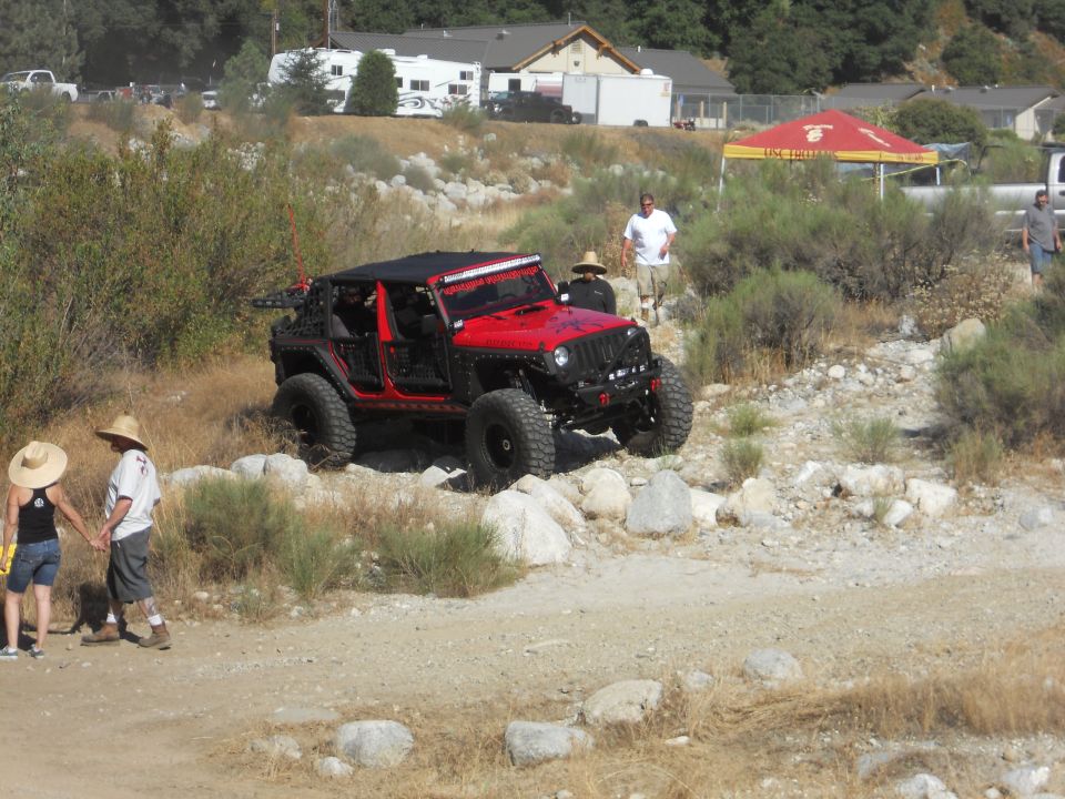 Red Jeep Wrangler with custom off-road modifications navigating rocky terrain