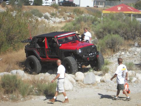 1986 Ford Bronco - A modified red Jeep Wrangler is shown off-road with several people observing the vehicle.