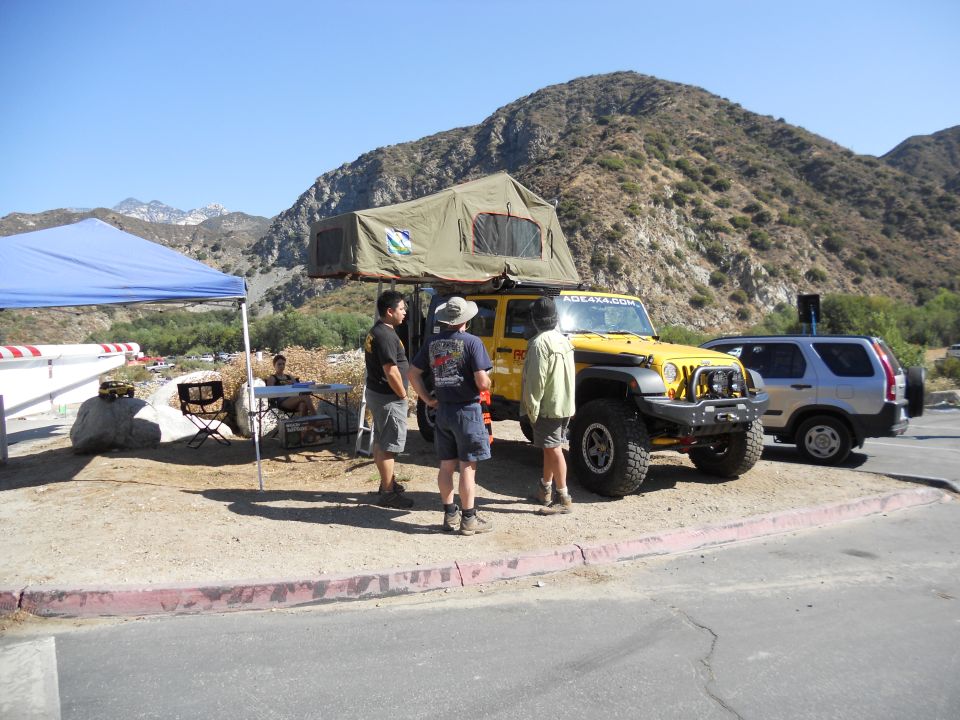 Yellow Jeep Wrangler with rooftop tent and silver Honda CR-V parked on dirt lot