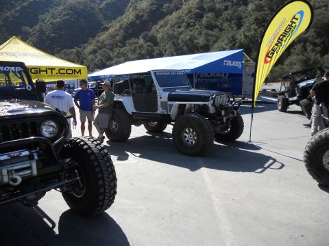 1986 Ford Bronco - Several off-road vehicles are displayed at an outdoor event with vendor tents and promotional flags.