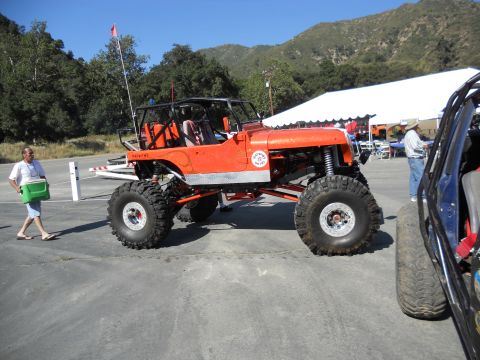 1986 Ford Bronco - An orange off-road vehicle with oversized tires and a roll cage is seen parked outdoors, with another vehicle partially visible to the righ…