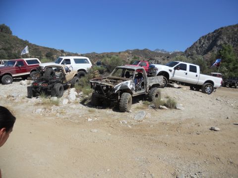 1986 Ford Bronco - A group of off-road vehicles are gathered on a dusty, hilly terrain under a clear blue sky.