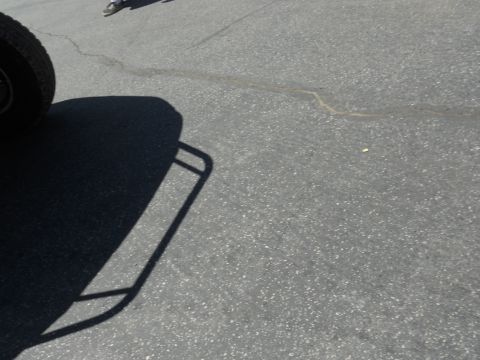 1986 Ford Bronco - A partial view of a vehicle's tire and its shadow on a cracked asphalt surface.