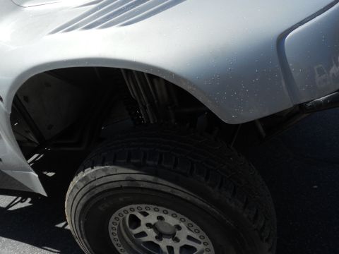 1986 Ford Bronco - Close-up view of the fender and tire of a white off-road vehicle, showing custom wheels and suspension components.