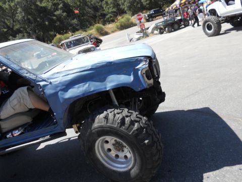 1986 Ford Bronco - A heavily modified blue truck with oversized tires sits parked outdoors, with other vehicles and spectators visible.