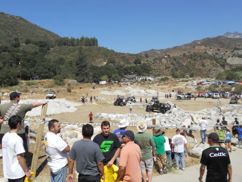 1986 Ford Bronco - A crowd gathers at an outdoor event with numerous off-road vehicles present in a rocky, mountainous terrain.