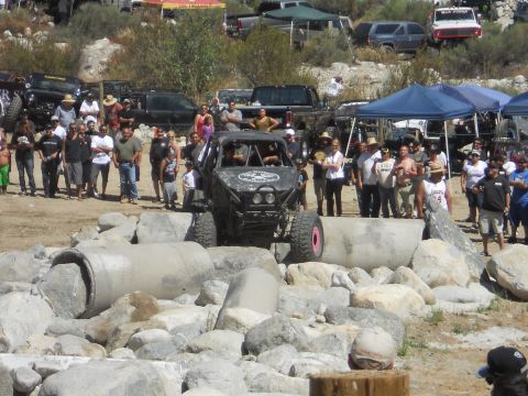 1986 Ford Bronco - Spectators watch as a custom off-road buggy tackles a challenging obstacle course made of large rocks and concrete pipes.