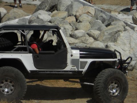 1986 Ford Bronco - Off-road modified Jeep Wrangler TJ with custom roll cage and large tires navigates rocky terrain.