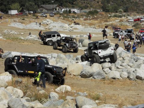 1986 Ford Bronco - Several modified Jeep Wranglers tackle a challenging off-road course with spectators watching.