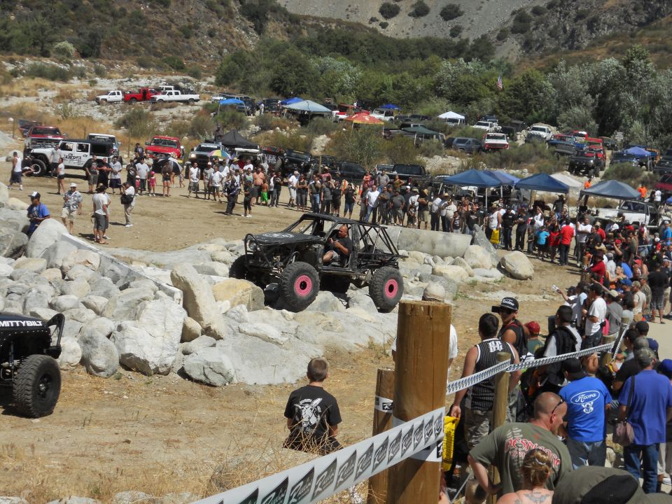 Off-road buggy with pink wheels on rocky terrain, crowd watching
