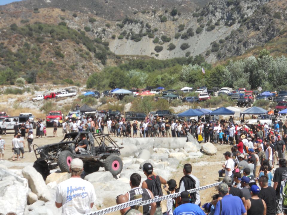 Custom off-road buggy with pink wheels navigating rocks, crowd watching