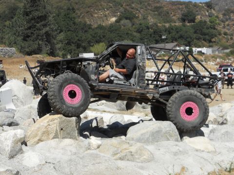 1986 Ford Bronco - A heavily modified off-road vehicle navigates a rocky terrain with a driver at the wheel.