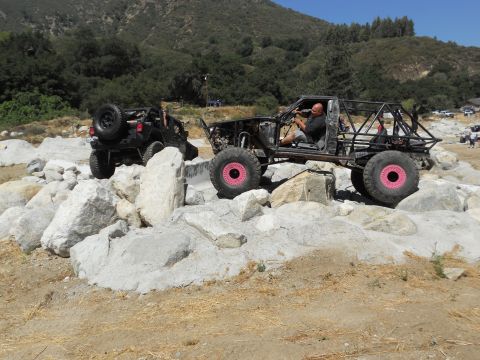 1986 Ford Bronco - Custom off-road vehicles tackle a challenging rocky obstacle course on a sunny day.