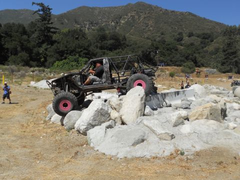 1986 Ford Bronco - A heavily modified off-road vehicle tackles a rocky obstacle course on a sunny day.