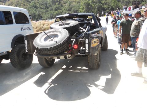 1986 Ford Bronco - Race truck with spare tires on rear bumper, seen at an event with spectators.