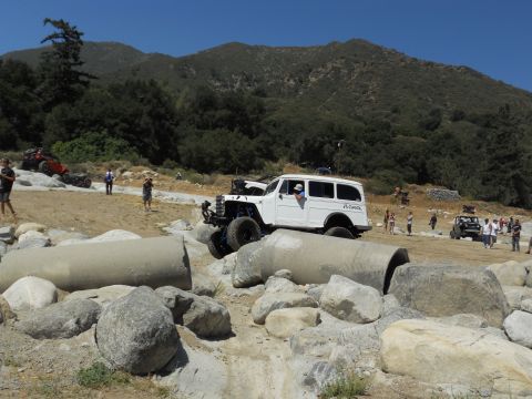 1986 Ford Bronco - A white off-road wagon is seen maneuvering through a challenging obstacle course with spectators in the background.