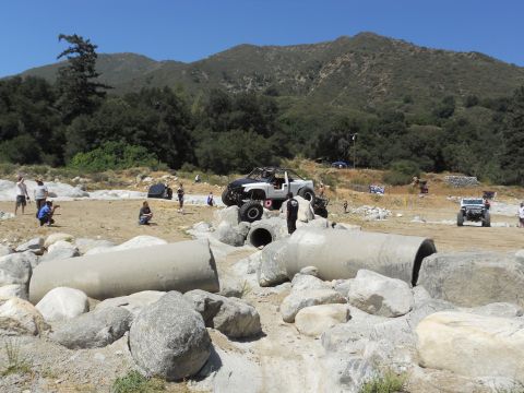 1986 Ford Bronco - A modified off-road truck tackles a challenging obstacle course with spectators and other vehicles present.