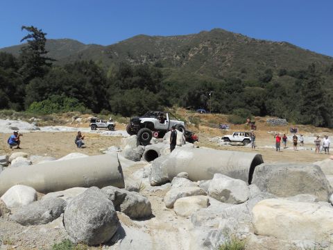 1986 Ford Bronco - Multiple off-road vehicles are seen navigating a challenging obstacle course on a sunny day.