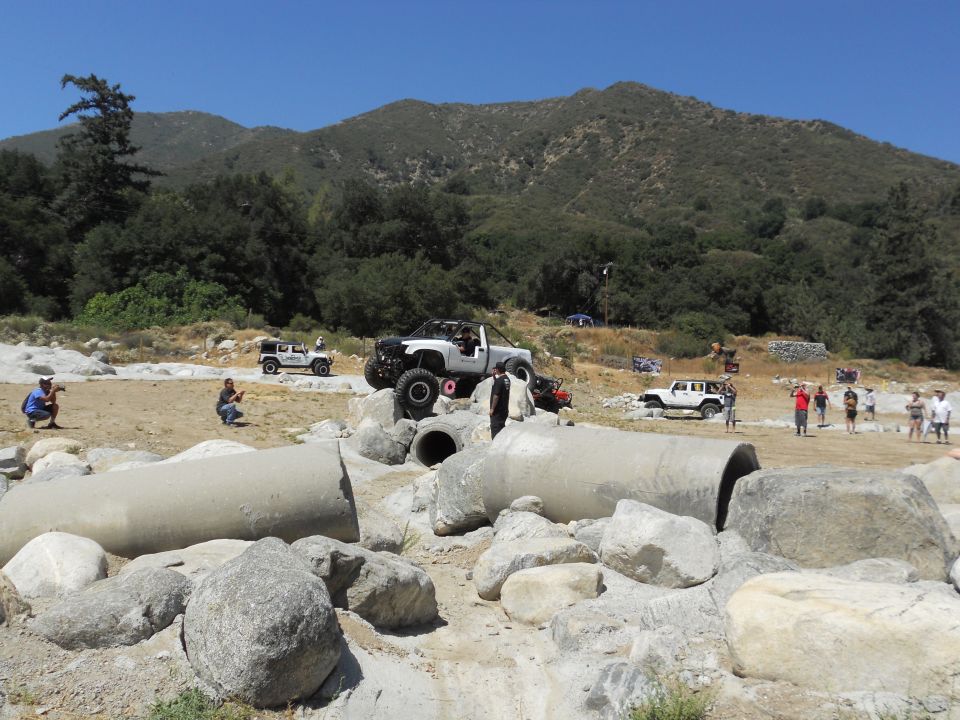 Off-road vehicles on a rocky course with large concrete pipes and hills in background