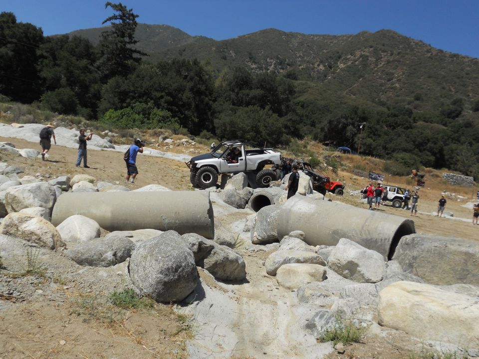 Off-road vehicles on rocky terrain with concrete pipes, people watching