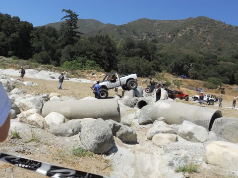 1986 Ford Bronco - Off-road vehicles tackle a challenging course with large concrete pipes and rocks.