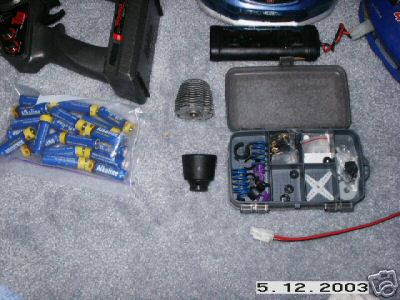 1998 Mercury Sable - A collection of remote control car parts, including an engine, batteries, and a small parts organizer, are laid out on a textured surface.