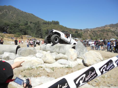 1986 Ford Bronco - A modified white truck navigates a rocky obstacle course with spectators watching.