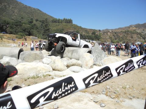 1986 Ford Bronco - A modified white truck attempts a challenging course with spectators watching.