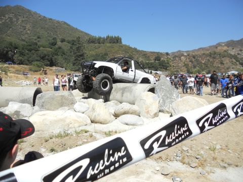 1986 Ford Bronco - An off-road truck navigates a challenging obstacle course during an event, with a crowd gathered to watch the action.