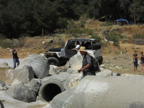 1986 Ford Bronco - A Jeep Wrangler is driven over large rocks and concrete pipes in an outdoor off-road area.